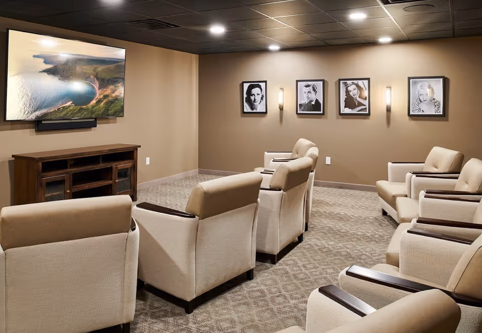 A small theater-style lounge with beige upholstered recliners facing a wall-mounted TV and framed black-and-white portraits on the back wall.