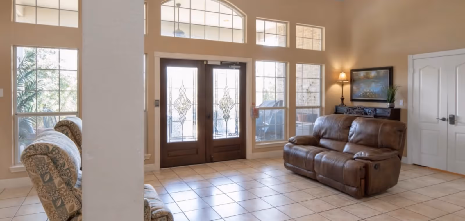 Bright entry living room with tiled floor, decorative double glass doors, large windows and two sofas.