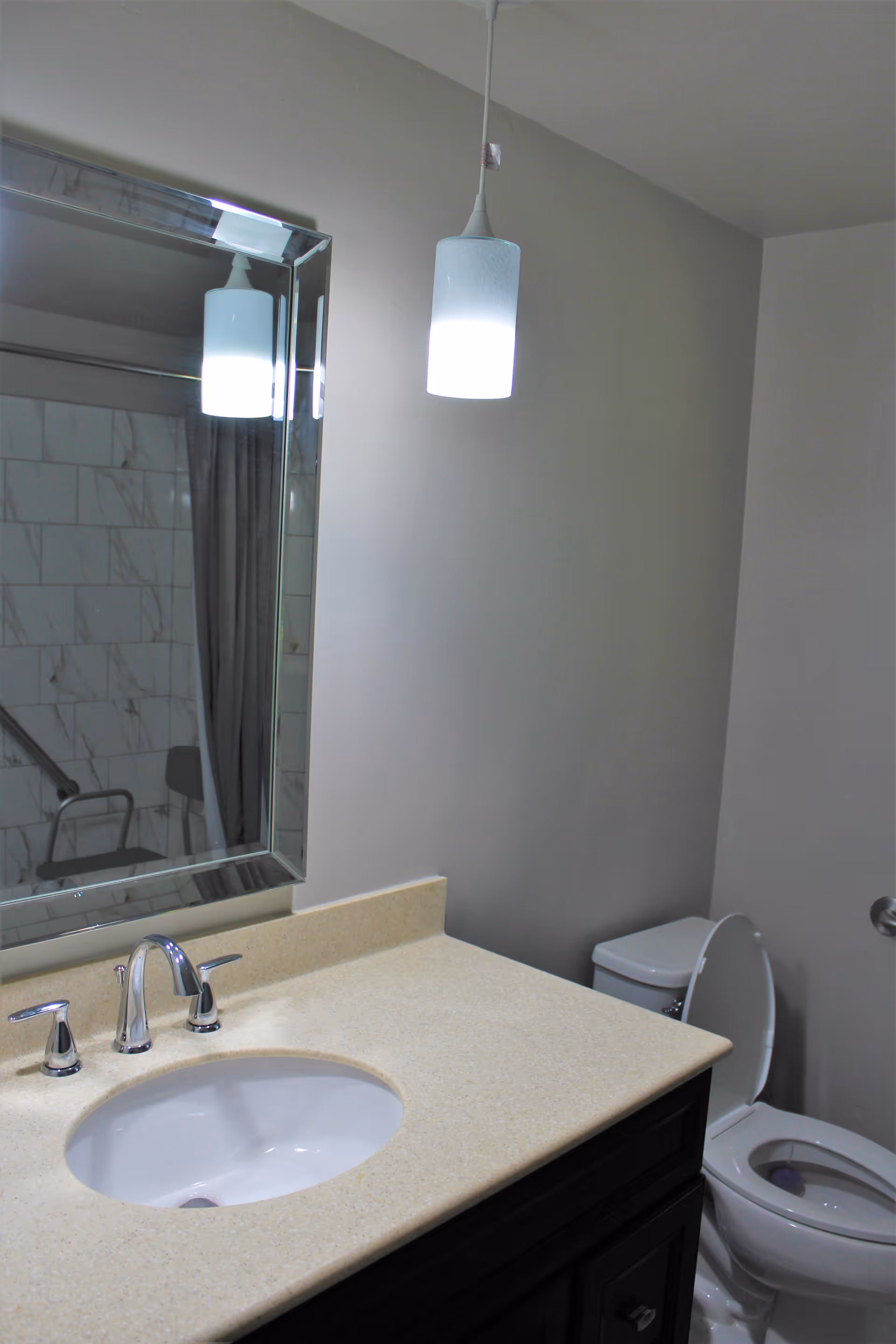 Bathroom vanity with sink and mirror, a hanging pendant light, and a toilet beside a tiled shower.