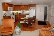 Open-plan living area showing a kitchen with wooden cabinets, a small round dining table, and upholstered chairs.