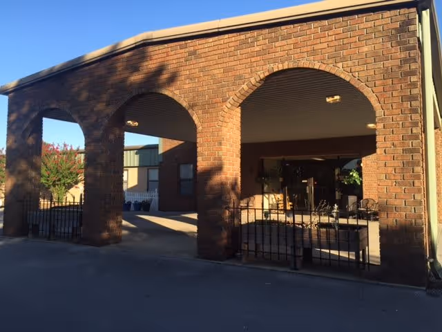 Brick building entrance with arched portico and a small gated seating area under the covered entry.
