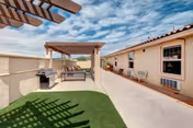 Outdoor patio area at Life Spire Assisted Living Rio Rancho featuring a pergola with seating underneath, a barbecue grill, artificial grass, and a walkway alongside the building under a partly cloudy sky.