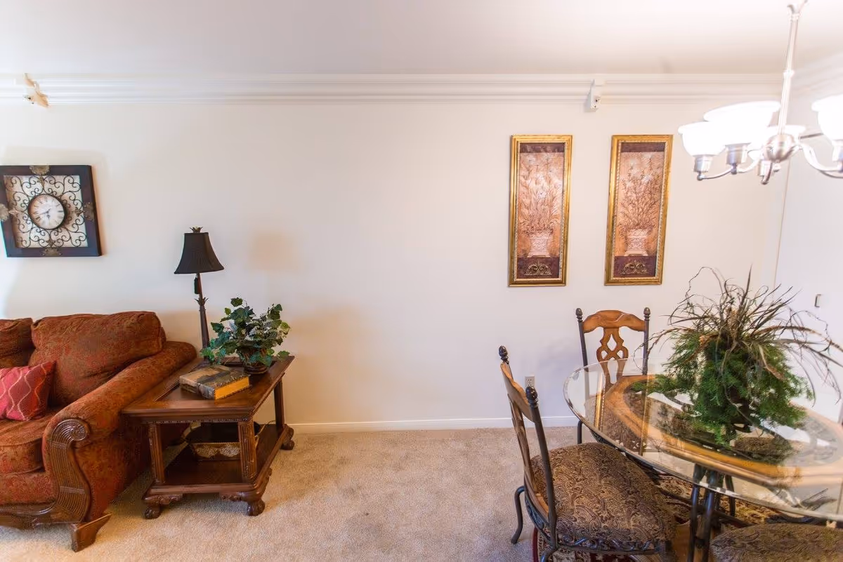 Cozy living and dining area with a sofa and side table on the left and a glass-top dining table with chairs and wall art on the right.