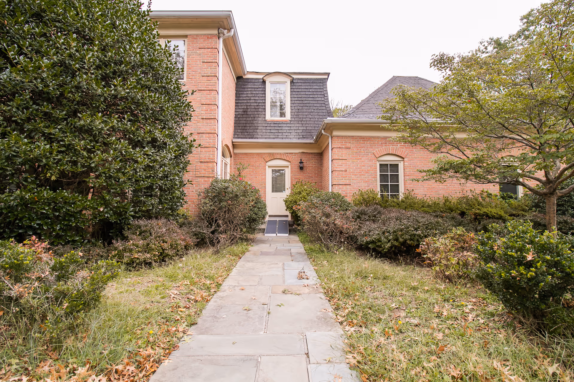 Stone walkway leading through shrubs to the front door of a two-story brick residential building.