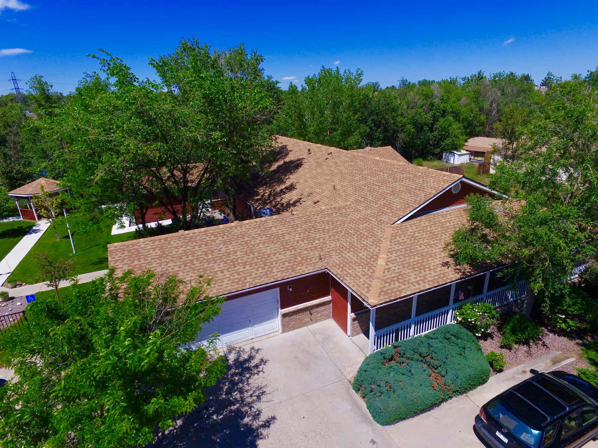 Aerial view of a single-story assisted living building with a tan shingled roof, garage driveway and surrounding trees.