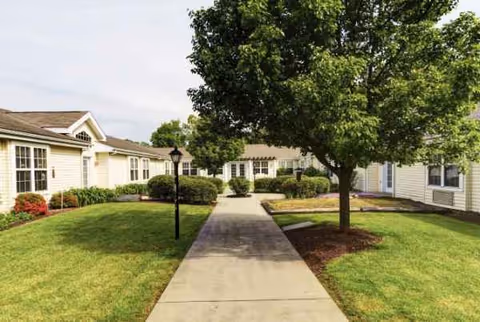 A concrete walkway runs between single-story senior living buildings with trees and green lawns.