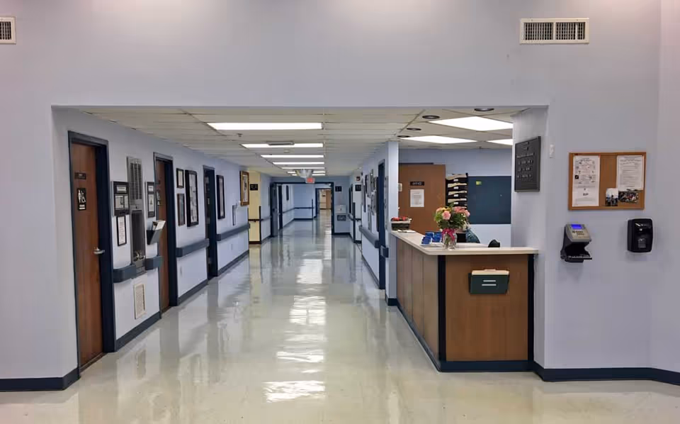 Long polished hallway inside a senior rehabilitation facility with a nurse's station on the right and patient room doors along the left.