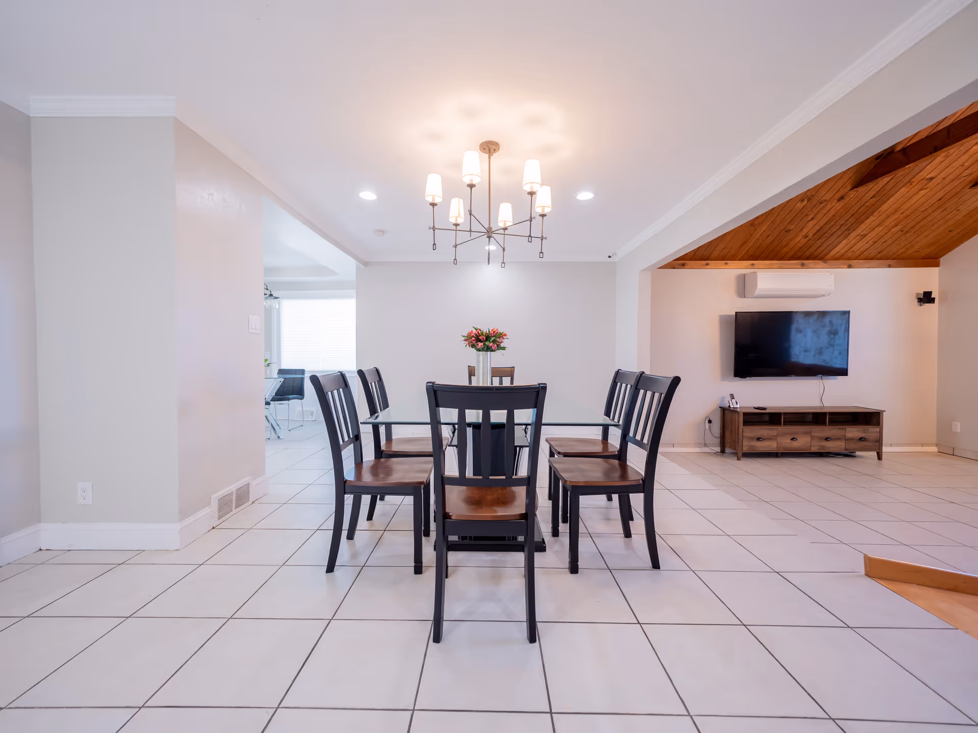 A spacious dining area with a glass-top table, multiple chairs, a chandelier, and a TV.