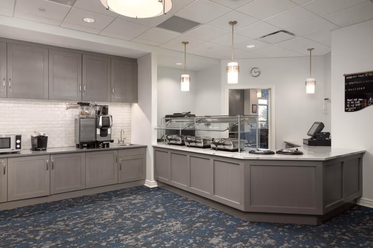 A clean serving counter and beverage station in a dining area with gray cabinetry, buffet warmers, and pendant lights.