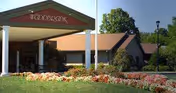 Front view of Woodbrook Assisted Living Residence building with entry columns and flowering landscaping.