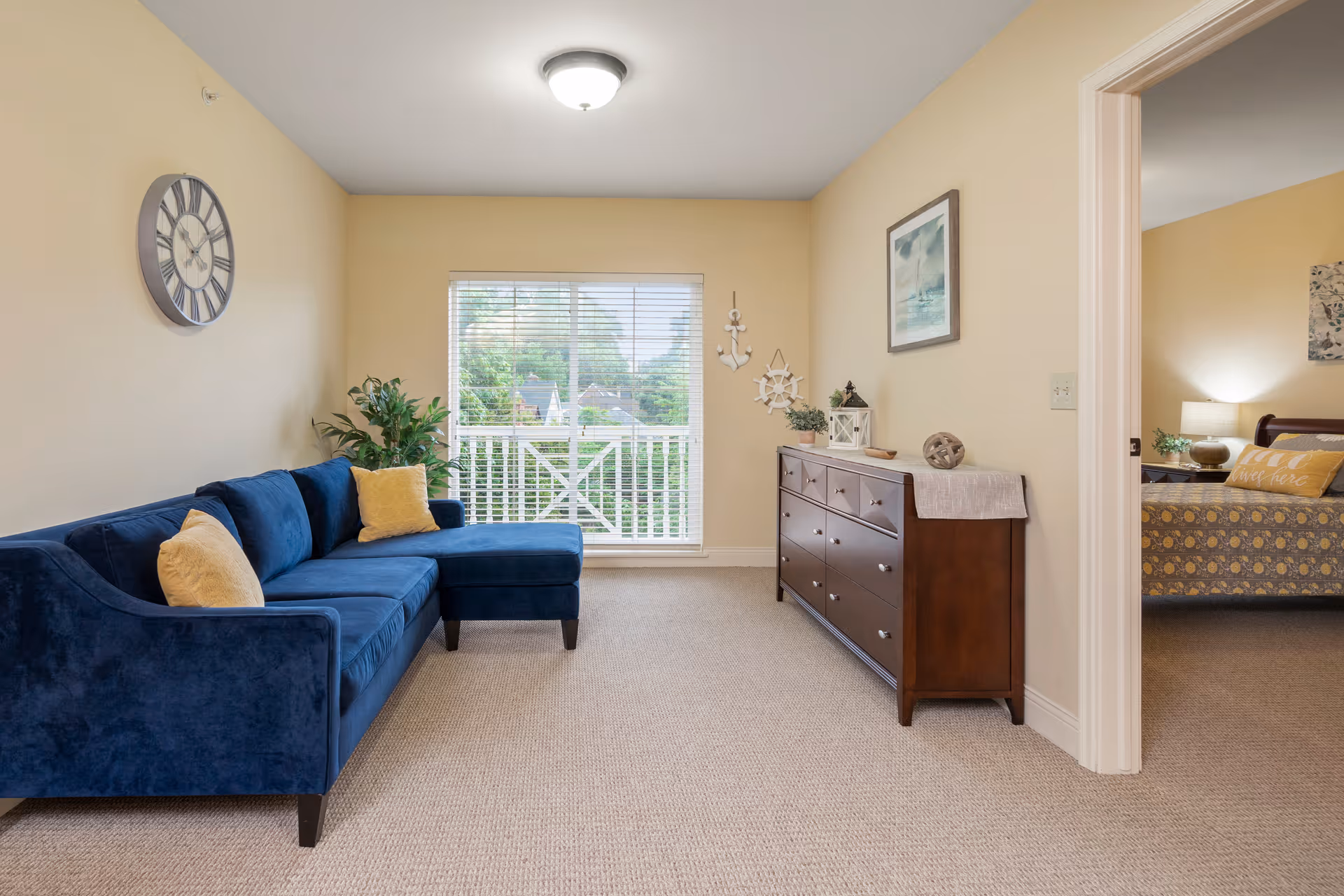 A bright living room featuring a blue sectional sofa, a wooden dresser, and a large window/door opening to a balcony.