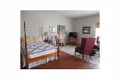 A furnished bedroom with a four-poster bed, chairs, and dresser in soft decor.