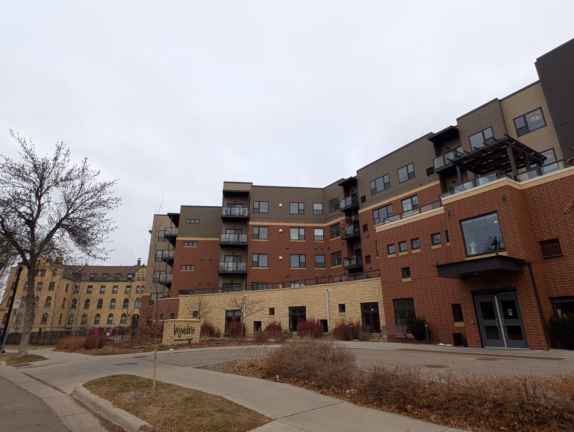 Exterior view of the Wyndris senior living building with brick and stone facade, balconies, entrance, and signage under an overcast sky.
