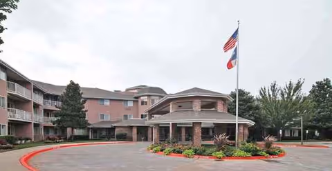 Exterior view of The Bentley Sky Active Living, showing entrance, circular driveway, and flagpole.