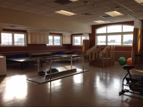 Bright rehabilitation gym in a senior facility with exercise equipment and stairs.