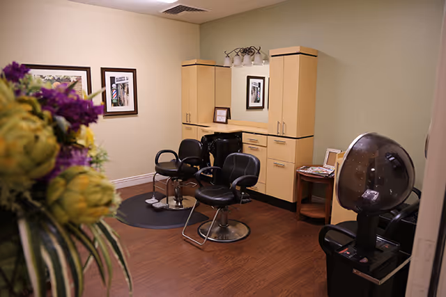Salon-style room with three styling chairs, a shampoo sink, cabinets, and a hooded hair dryer.
