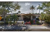 Front exterior of Homestead Manor with palm trees, landscaping, and two people near the entrance.