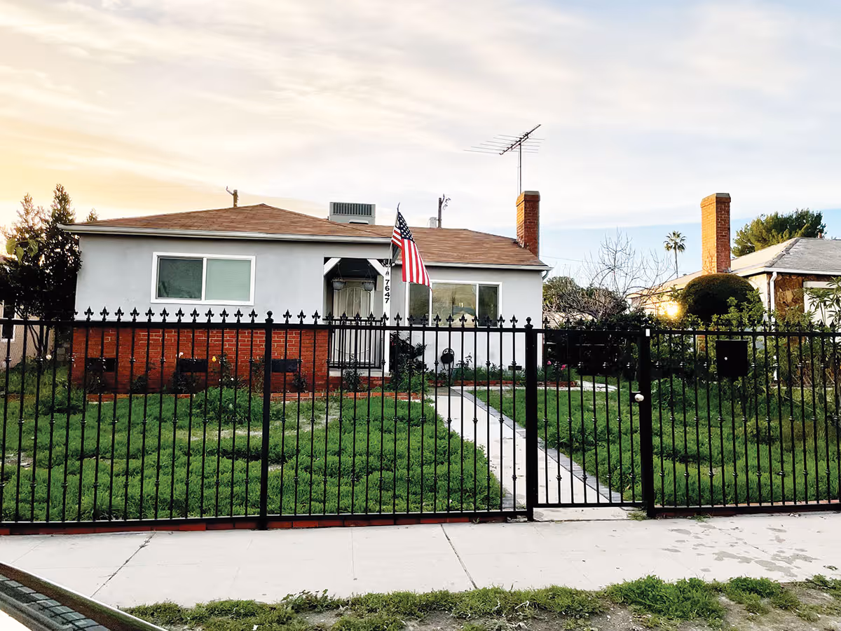 Single-story house with an American flag, a black metal fence and a grassy front yard with a walkway.