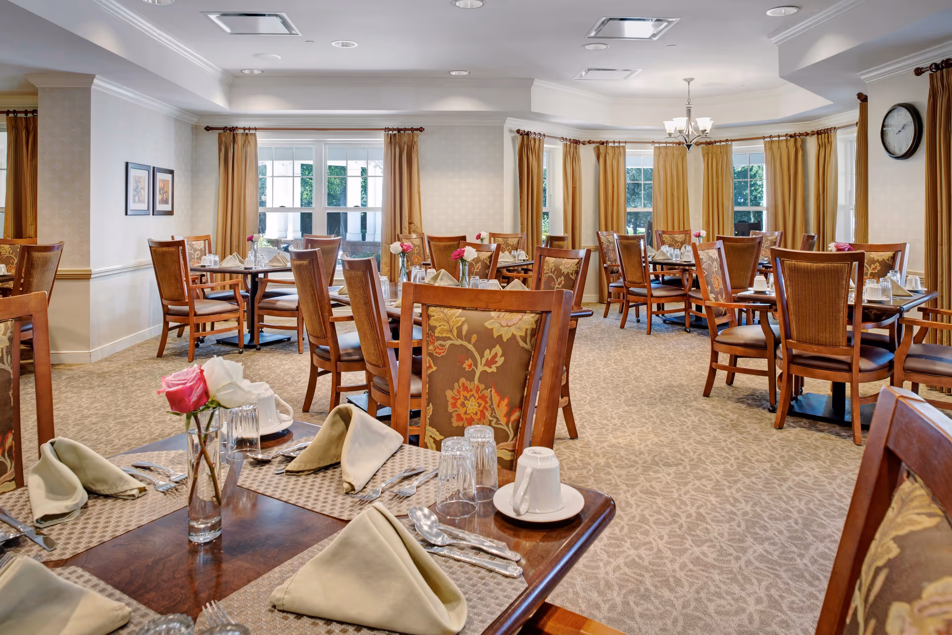 Bright, well-appointed dining room with multiple set tables, wooden chairs, and floral centerpieces.