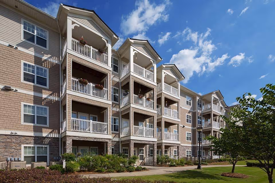 Multi-story residential building with stacked balconies, landscaped grounds, and a blue sky.