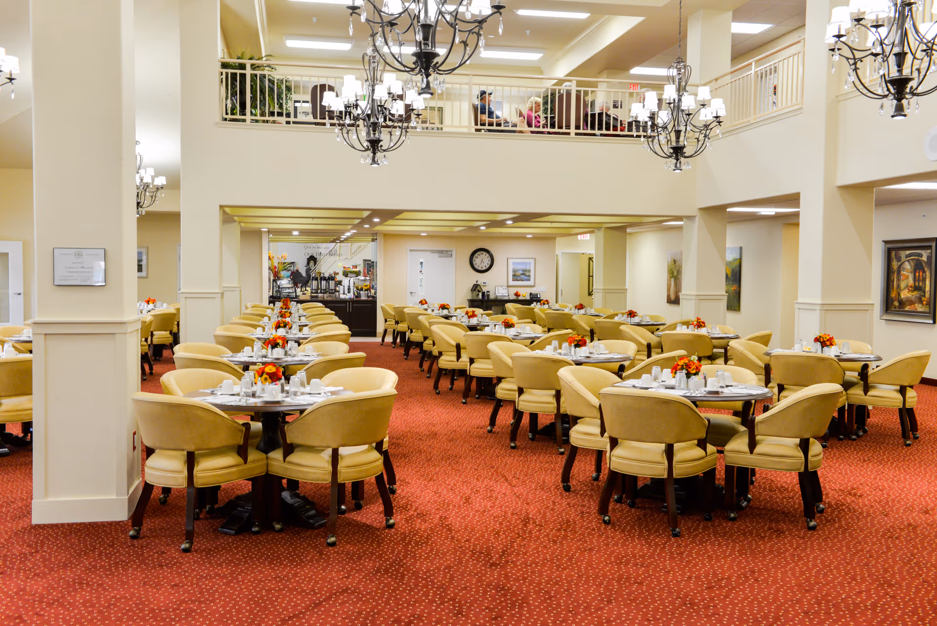Spacious dining room with multiple round tables and upholstered chairs, chandeliers, and a mezzanine balcony.