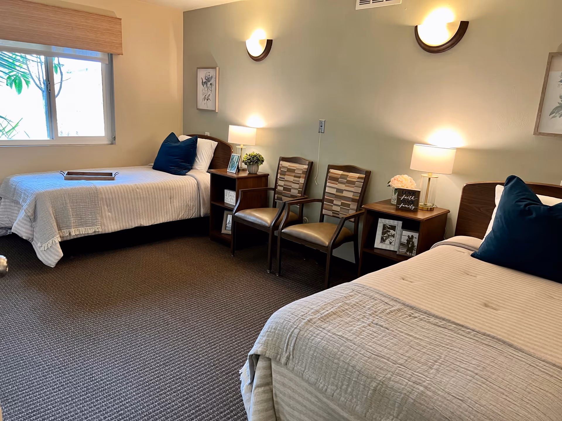 A bright, carpeted bedroom with two twin beds, bedside tables, lamps, and two chairs.