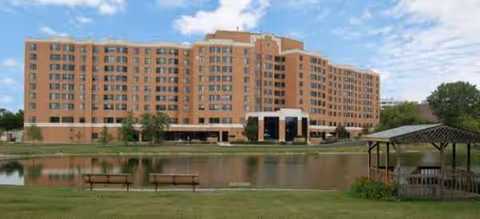Brick senior living building with pond, benches, and a gazebo in the front yard.