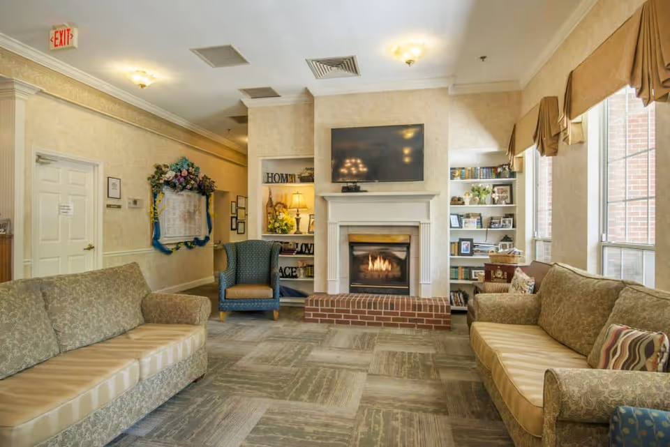 Cozy living room with sofas and armchairs arranged around a fireplace and TV, flanked by bookshelves and large windows.
