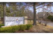 Outdoor view of the entrance sign for Brewster Place, surrounded by trees and shrubs with a building visible in the background.
