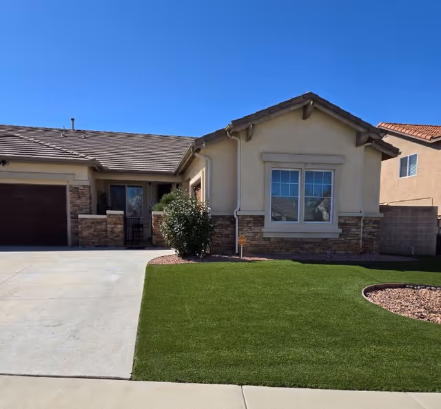 Single-story beige home exterior with stone accents, driveway, and manicured lawn.