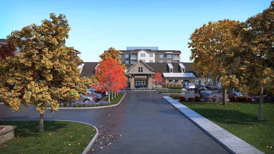Front exterior view of The Langford Methodist Retirement Community building with a driveway leading to the entrance, surrounded by trees with autumn foliage and parked cars.