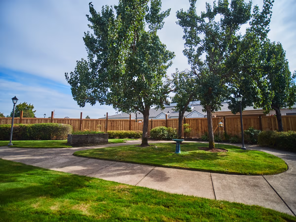 Well-maintained courtyard with paved walkways, green lawns, large trees, lamp posts and a wooden fence.