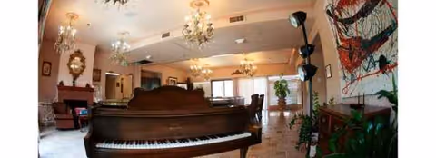 Cozy senior living lounge with grand piano, chandeliers, and comfortable seating.