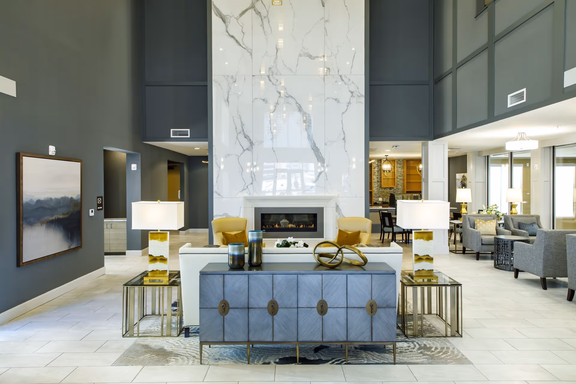 Bright modern lobby with a marble-clad central fireplace, seating groups, and high ceilings.