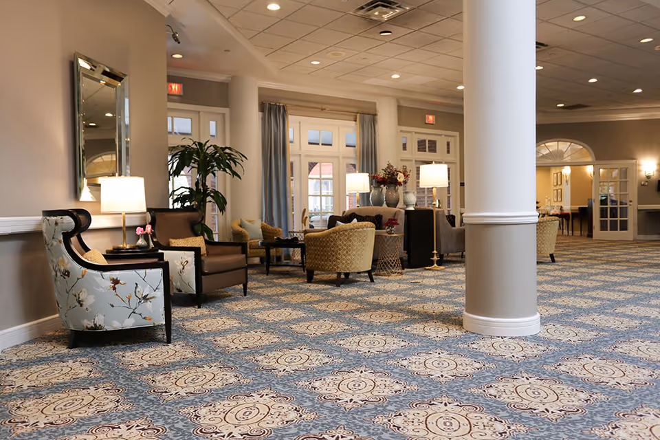 Lobby-style lounge with patterned carpet, columns, armchairs, side tables and lamps.