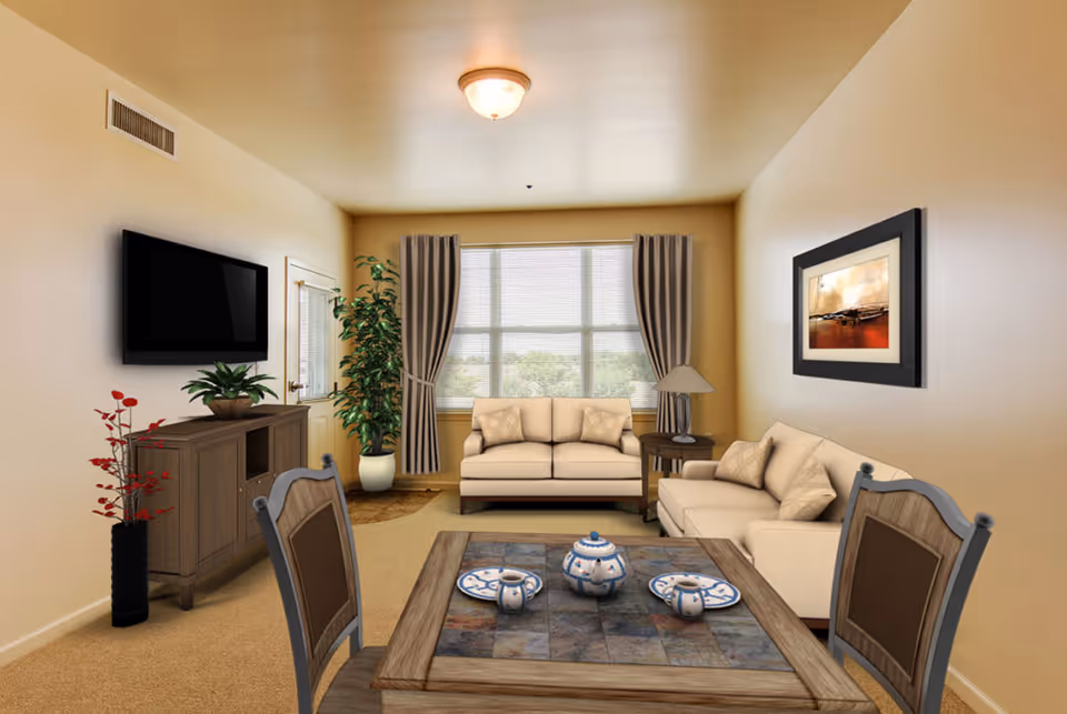 A cozy living room with beige walls and carpet, featuring two beige sofas with cushions, a wooden coffee table with a tea set, a wooden side table with a lamp, a large window with curtains, a flat-screen TV mounted on the wall above a wooden cabinet, and two potted plants.