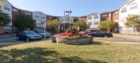 Brookdale Franklin exterior view showing a circular flower bed, grassy lawn, and parked cars.
