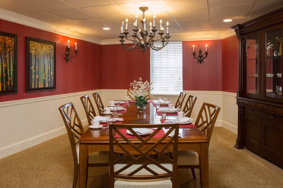 Formal dining room with a long wooden table set for a meal, chandelier, red walls, and a china cabinet.