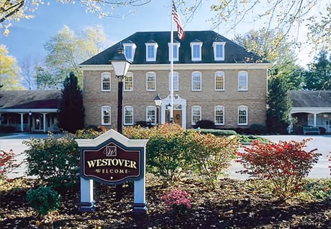 Front view of the brick Westover Retirement Community building with a flagpole and landscaped sign reading "Westover Welcome".