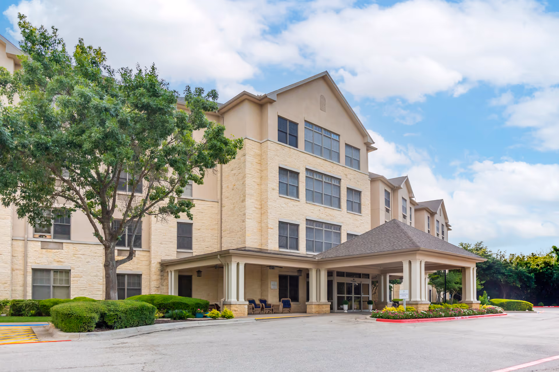 Exterior view of a multi-story beige senior living facility with a covered entrance.