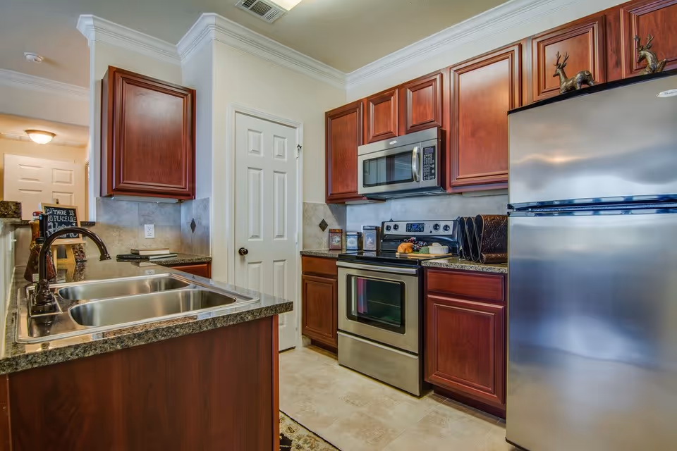 Modern kitchen with stainless steel refrigerator and oven, dark wood cabinets, granite countertops and a double sink island.