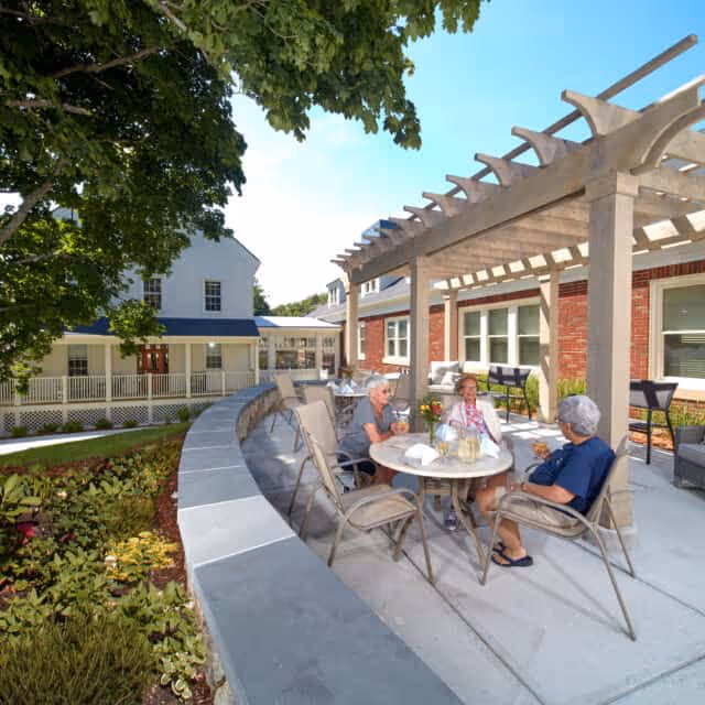 Three people seated around a table under a pergola in an outdoor courtyard of Forestdale Park Senior Living.