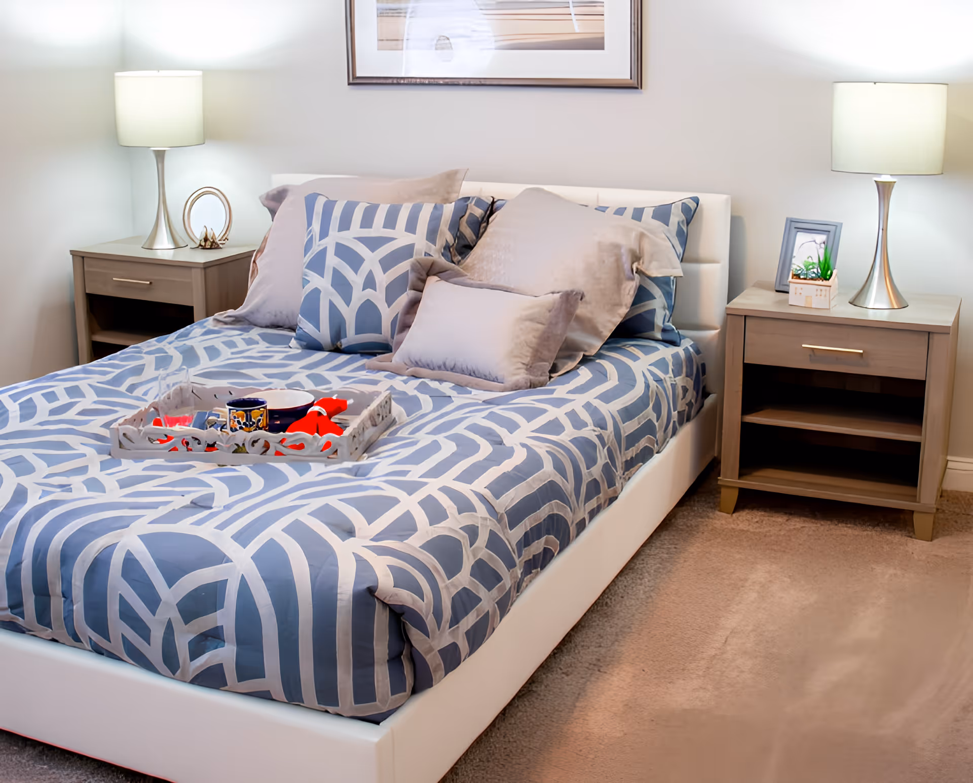 A neatly made bed with blue-gray geometric bedding, multiple pillows, two nightstands and lamps in a bedroom.