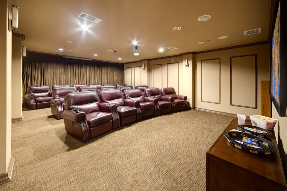 A private screening room with rows of burgundy leather recliners, a ceiling projector, and a snack table.