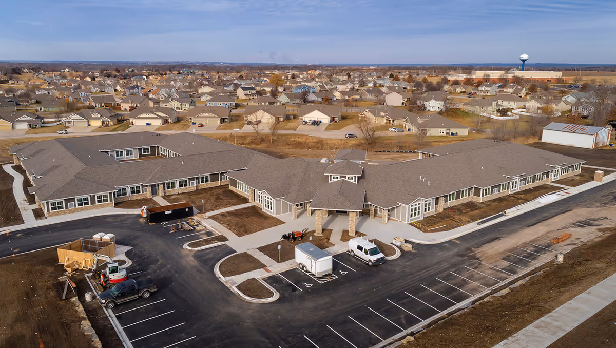 Aerial view of a single-story assisted living and memory care facility with a parking lot and surrounding residential neighborhood.