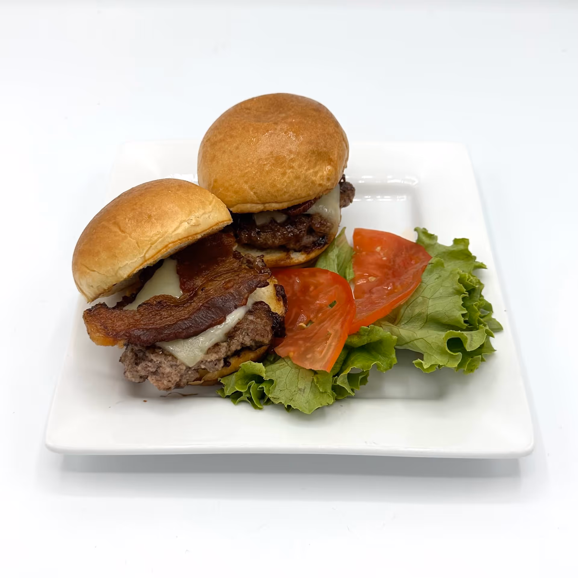 Two bacon cheeseburger sliders with lettuce and tomato on a white square plate.