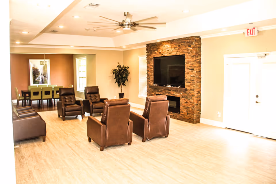 A spacious senior living lounge with leather seating, a stone fireplace, and a mounted TV.