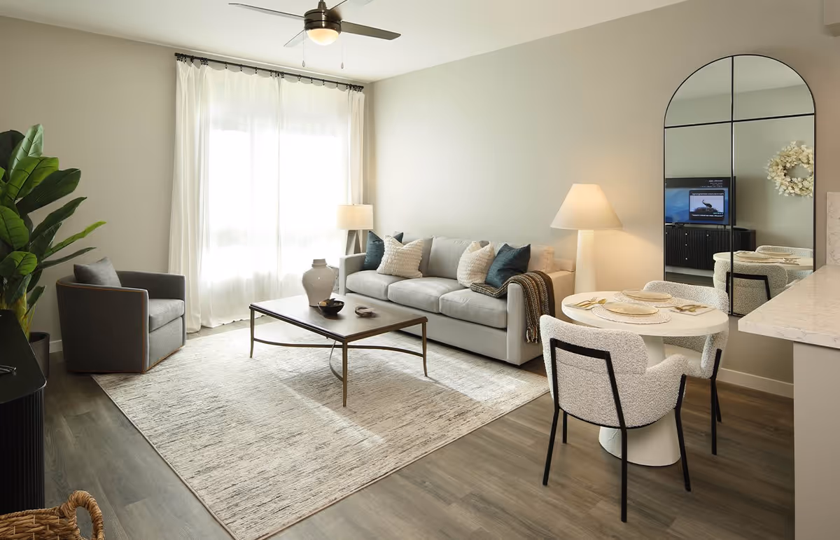 Bright modern living room with a sofa, armchair, coffee table, small dining table and large arched mirror.