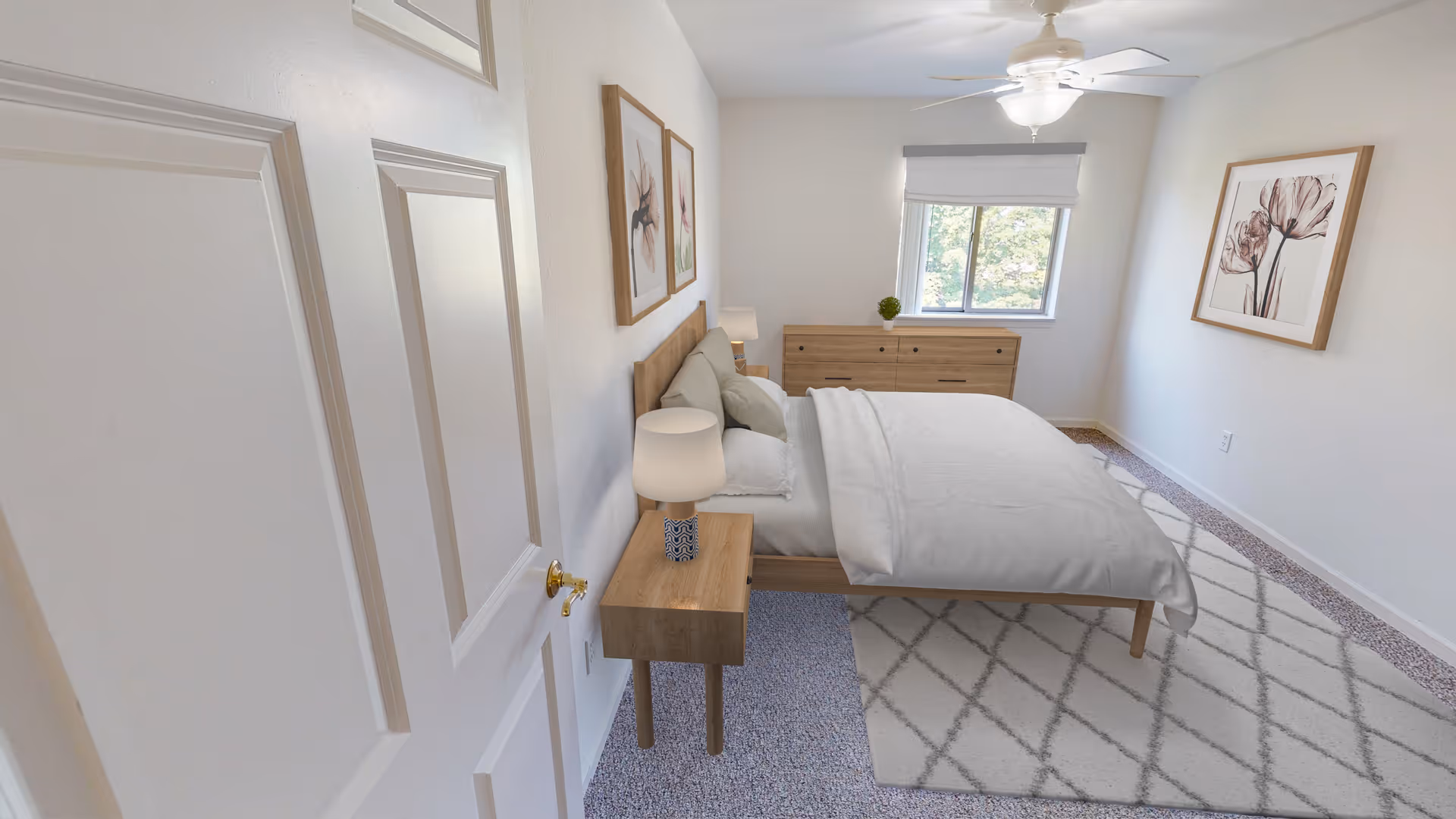 Bright, minimal bedroom with a bed, wooden nightstand and dresser, ceiling fan, area rug, and framed wall art.