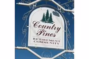 Decorative hanging sign reading "Country Pines Retirement Community" with pine tree graphic against a blue sky.